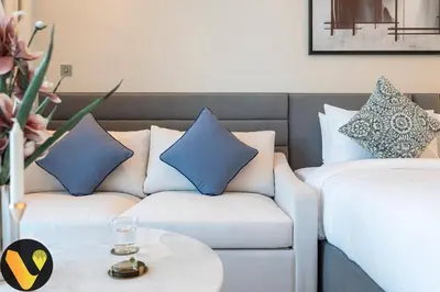 a white couch with blue pillows in a hotel room at Vogue Downtown The Sterling by Omniyat, near Burj Khalifa and Dubai Mall, Studio Apartment with Balcony and Access to all Amenities in Dubai