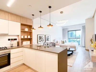 a kitchen with white cabinets and a living room at Rokane G25 Studio Modern Comfort with City Views in Dubai