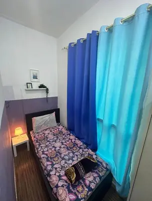 a small bedroom with a bed with blue curtains at Partition Room with window Near Mashreq Metro in Dubai