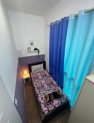 a small bed in a room with blue curtains at Partition Room with window Near Mashreq Metro in Dubai