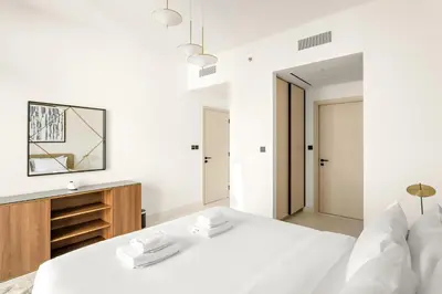 a white bedroom with a large bed and a wooden dresser at Silkhaus Beachside Spacious 2BDR in Marina Vista in Dubai