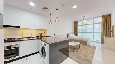 a kitchen with white cabinets and a living room at Modern Furnished Studio in Dubai