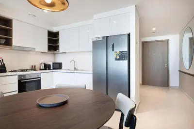 a kitchen with a wooden table and a refrigerator at Downtown Chic 2 Bedroom Apartment I Dubai Mall Access I Views of Burj Khalifa from Pool I Free Parking, Gym, Pool & Wi-Fi I by Meerak in Dubai