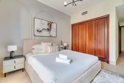 a bedroom with a large white bed with a wooden cabinet at GuestReady - Downtown oasis with Burj Khalifa view in Dubai