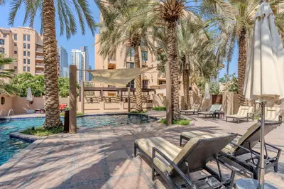 a pool with palm trees and chairs and a hammock at GuestReady - Downtown oasis with Burj Khalifa view in Dubai