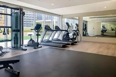 a gym with treadmills and ellipticals in a room with windows at Keyrock Living - 1BR at Reva Residence with Lake View in Dubai