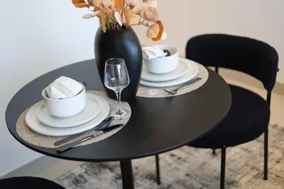 a black table with plates and a vase with flowers at Cosy Studio in Binghatti House in Dubai