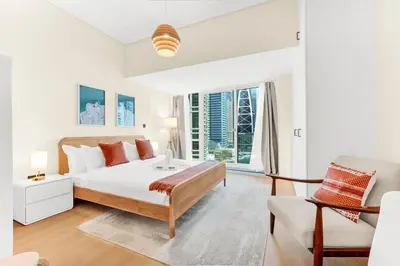 a white bedroom with a bed and a chair at Waves - Modern Studio with Stunning Lake Views in JLT in Dubai