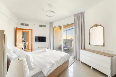 a white bedroom with a large bed and a mirror at Luxury 1BR with Lake View Near Downtown Balcony and Pool Access in Dubai