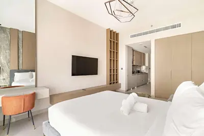 a white bedroom with a large bed and a tv at Modern Studio with rooftop pool and gym in JVC in Dubai