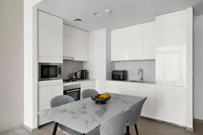 a kitchen with white cabinets and a table and chairs at 1BR Palace Residences, City View in Dubai