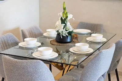 a glass table with chairs and white cups and a vase with flowers at Beautiful 2BR - Burj Views And Dubai Mall Connection in Dubai