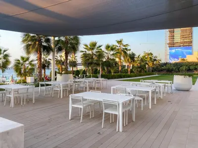 a row of tables and chairs on a patio with palm trees at Modern 1BR Apartment Steps from Beach and Dubai Nightlife in Dubai
