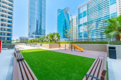 a park with benches and a playground with tall buildings at Keyrock - Zada Tower, Business Bay Lake-View Apartment in Dubai