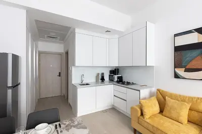 a kitchen and living room with white cabinets and a couch at Luma Studio in Jumeirah Village Circle in Dubai