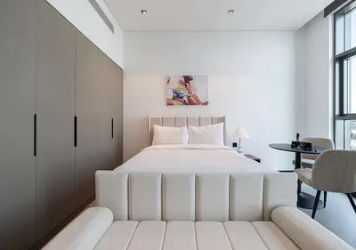 a white bedroom with a large bed and a table at Chic Studio with Top Amenities in Dubai