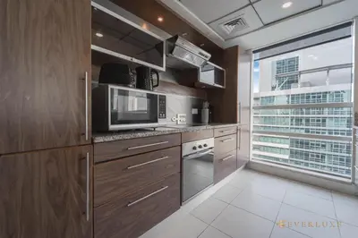 a kitchen with wooden cabinets and a microwave at Beautiful & Spacious 3 Bedroom Wmaids In Marina in Dubai