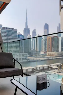 a chair and two mugs on a glass table on a balcony at Cozy 1BR apartment Binghatti Canal Business Bay in Dubai