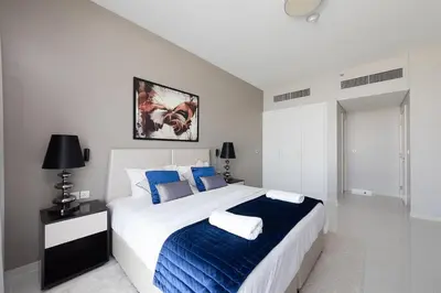a white bedroom with a large bed with blue pillows at Modern 1BR apartment Artesia DAMAC Hills in Dubai