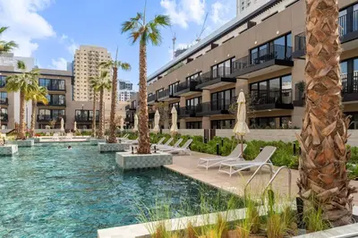 a swimming pool with chairs and palm trees in front of a building at Urban Studio With Pool & Tennis Court in Dubai