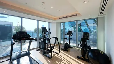 a gym with three cardio machines in a room with windows at Cozy 1BR with Canal View, Pool & Gym Access in Dubai
