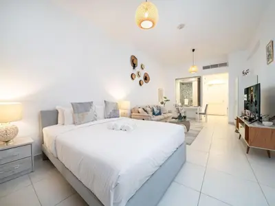 a white bedroom with a large bed and a living room at Chic Waterfront Studio in Palm Views West in Dubai