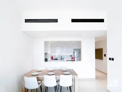 a dining room with a wooden table and white chairs at Elegant 2 Bedroom Apartment -Binghatti Emerald JVC in Dubai