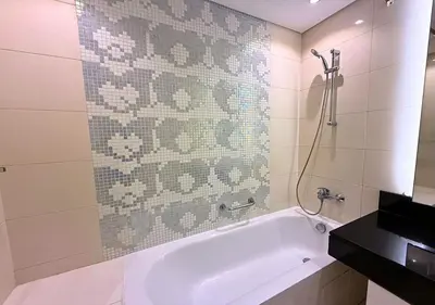 a white bath tub in a bathroom with a tile wall at Capital Bay Tower B Comfort Studio in Dubai