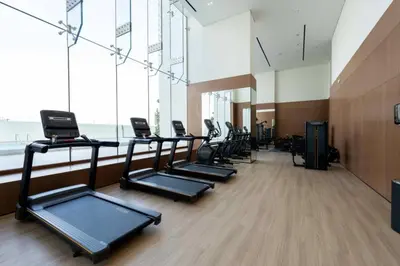 a gym with a row of treadmills and windows at Modern 1br In Jvc Balcony, Pool & Parking in Dubai