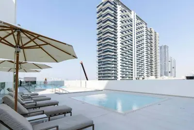 a pool with chairs and an umbrella and a building at Modern 1br In Jvc Balcony, Pool & Parking in Dubai
