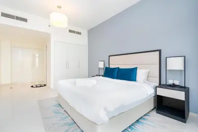 a white bedroom with a large bed with blue pillows at Ahlan HH - Luxury 2BR Damac Tower 108 at High Floor in Dubai