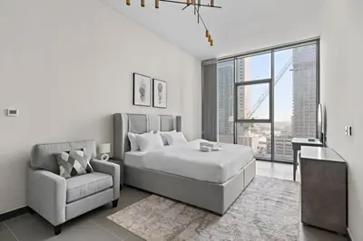 a white bedroom with a bed and a chair at Stonetree - Cozy 1 BR at MBL Near Metro in Dubai