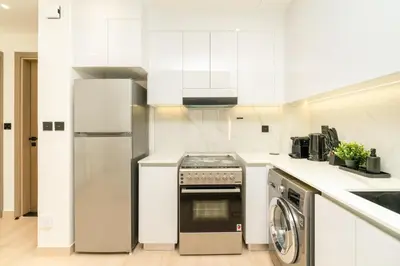 a white kitchen with a refrigerator and a dishwasher at Luxury 1BR Apartment in JVC with Stunning Pool in Dubai