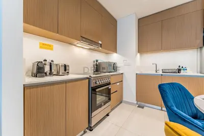 a kitchen with wooden cabinets and appliances and a table at Community View 2BR with Balcony, Surf at Creek Beach Building 2, Creek Harbour by Deluxe Holiday Homes in Dubai