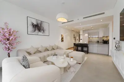 a white living room with white furniture and a kitchen at Daniels 1BR at Waves Grande In Sobha Hartland in Dubai
