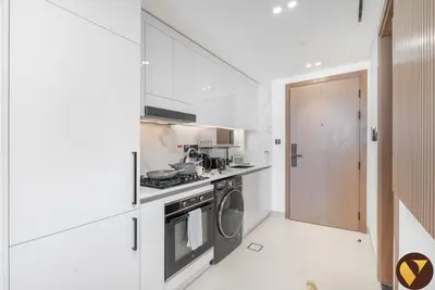 a white kitchen with a stove and a washing machine at Vogue JVC Binghatti Galaxy near Circle Mall, Studio Apartment with Balcony and City View, Access to all Amenities in Dubai