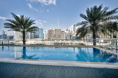 a large swimming pool with a city skyline in the background at 1BR Stunning Canal & Burj view, Luxury Stay at Fairview Residency in Dubai