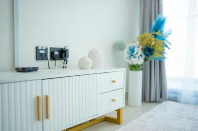 a white dresser in a room with a vase of flowers at AWS Holiday Homes - Perfect Dubai Stay! in Dubai