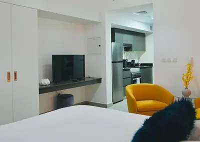 a room with a bed and a yellow chair and a kitchen at Fully Furnished Elegant Studio Apartment Close by Dubai Science Park, Dubai Miracle Garden, Butterfly Garden and Dubai Hills Mall in Dubai