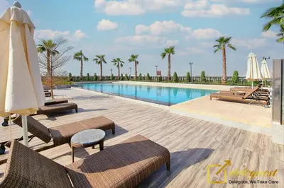 a pool with chairs and an umbrella and palm trees at Tranquil 3br Townhouse in Damac Hills2 by deleguest in Dubai