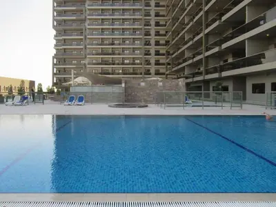 a large swimming pool with blue chairs and a tall building at Modern Studio Retreat in Sports City Dubai in Dubai