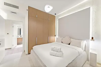 a bedroom with a large white bed with a wooden headboard at Luxe 1BR in Orchid Creek with Balcony Pool & Gym in Dubai