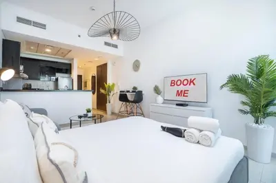 a white bedroom with a white bed and a book me sign at SUNRISE HOMES - A Modern Studio near JBR Beach in Dubai