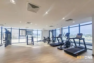 a gym with treadmills and ellipticals in a room with windows at Exquisite Living in Riviera One Bedroom in Dubai
