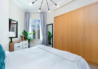 a bedroom with a white bed and a wooden cabinet at Bespoke Holiday Homes - 2BR Apartment with Riva Beach Club Access, Al Nabat in Dubai