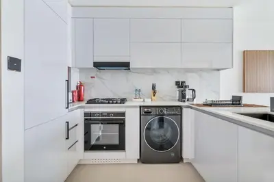 a white kitchen with a washing machine in it at Lovely 1BR flat wBalcony Gym & Pool in JVC in Dubai