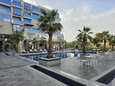 a resort with a pool and palm trees and tables and chairs at Elite Business & Family Turnkey 433 Residence 2BR in OIA Motor City in Dubai