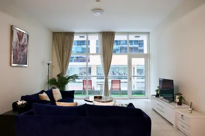 a living room with a blue couch and a large window at Nivis find-Affordable & Spacious 1 BHK- 10 Mins to Dubai Mall in Dubai