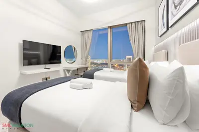 a white hotel room with a large bed and a television at SML Vacation Homes - Sky High Apartments with Burj Khalifa and Dubai Fountain Views at Grande Signature, Downtown Dubai in Dubai