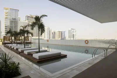 a pool with chaise lounges and palm trees in a city at Modern Studio at Upside Living with Burj Views - Business Travelers in Dubai